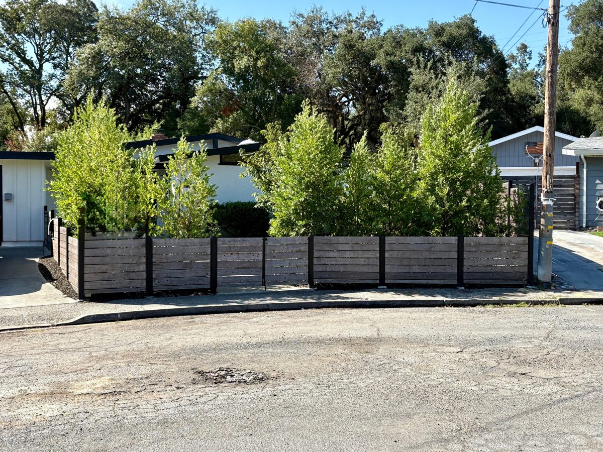 Pothole of broken asphalt in front of a home with a wood fence